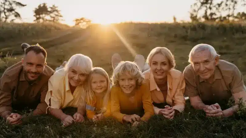 A group of six people lies on the grass, enjoying a golden sunset in a serene outdoor setting
